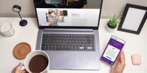 A person sits at a desk looking at laptop and smartphone versions of a website.