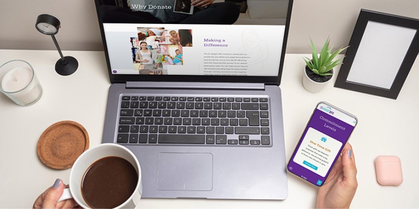 A person sits at a desk looking at laptop and smartphone versions of a website.