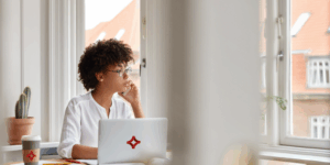 A woman sits at her desk with a laptop featuring the logo of SJC on the cover.
