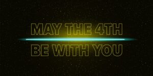 A lightsaber glows across lit words that say "May the 4th be with you."