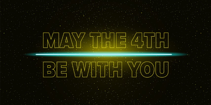 A lightsaber glows across lit words that say "May the 4th be with you." 