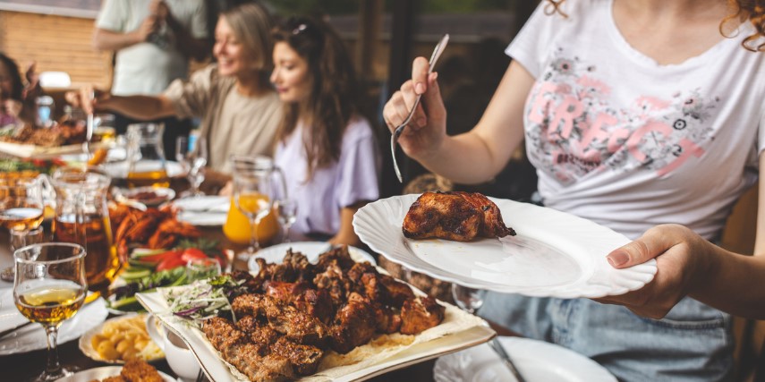 Friends gathered around a table filling their plate with grilled foods.