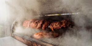 Slabs of meat surrounded in smoke inside a charcoal smoker.