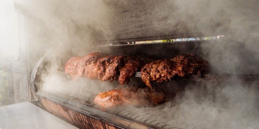 Slabs of meat surrounded in smoke inside a charcoal smoker.