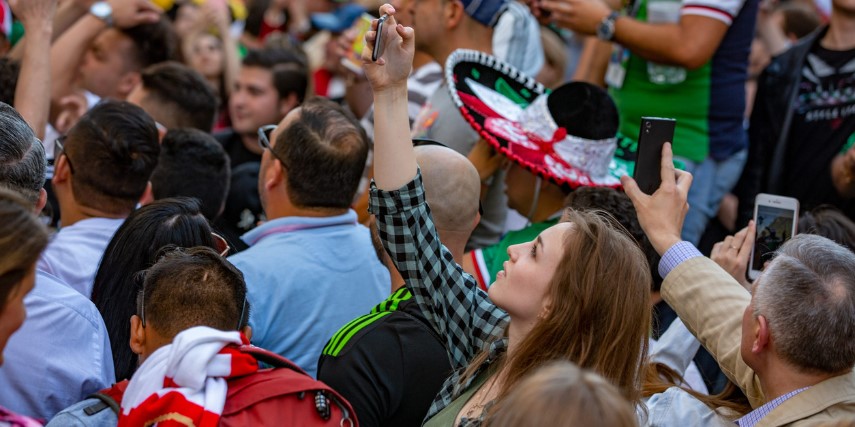 A crowd of people look up and one woman records the scene on her smartphone.