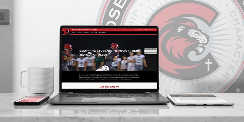 A laptop sits on a desk showing a new website for a private school with the school's logo in the background.