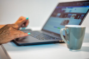 Woman hands using laptop with cup of coffee on the side, lateral view.