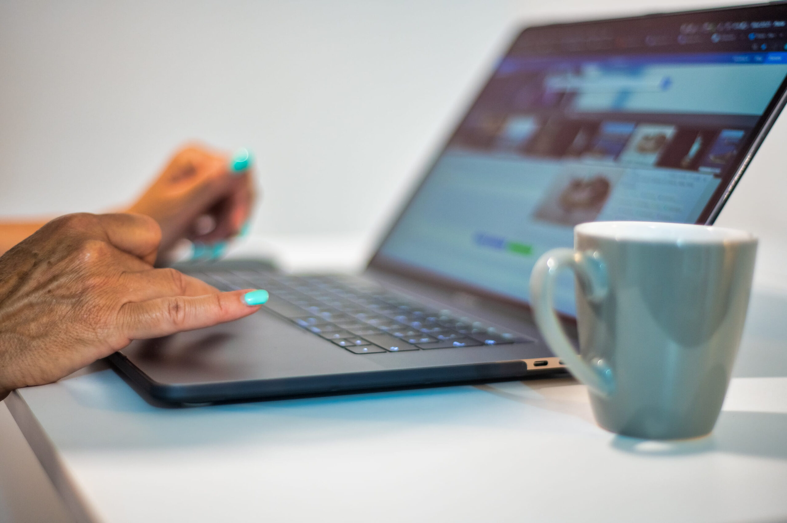 Woman hands using laptop with cup of coffee on the side, lateral view.