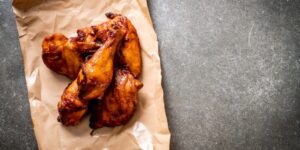 Several deep-fried chicken wings and drumsticks on a section of brown paper against a slate background.