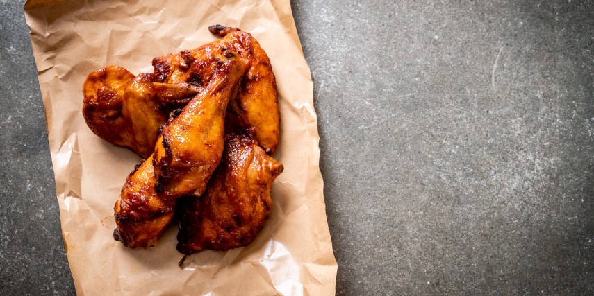 Several deep-fried chicken wings and drumsticks on a section of brown paper against a slate background.