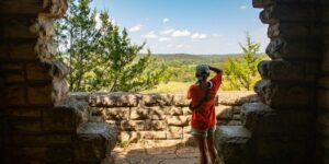 View from behind of a woman taking a picture of a valley.