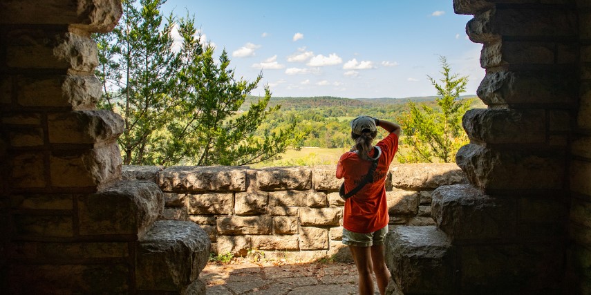 View from behind of a woman taking a picture of a valley.