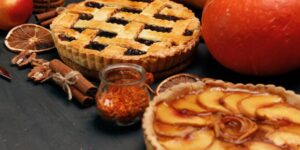 One lattice-top berry pie and a peace pie surrounded by cinnamon, apples and other ingredients.