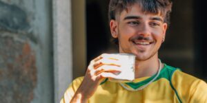A man in a yellow and green practice soccer jersey holds a cup of coffee.