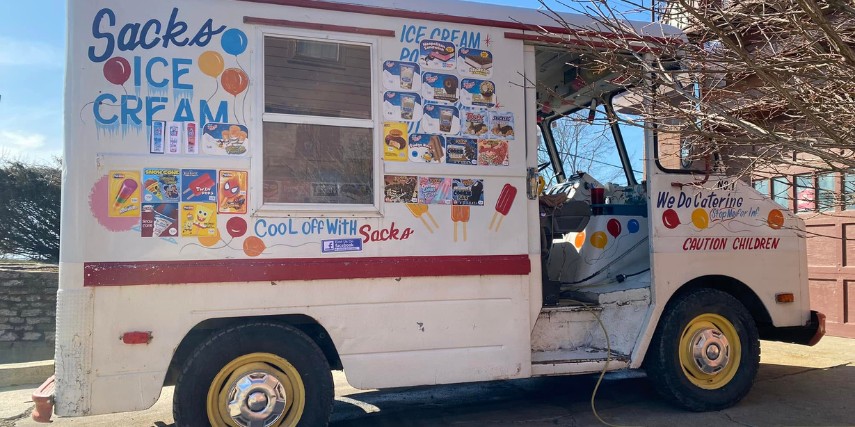 An old-fashioned ice cream truck with menu options displayed on the side near an ordering window.