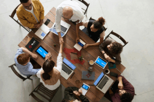 Aerial view of colleagues sitting at a table discussing partnership strategy surrounded by laptops and documents
