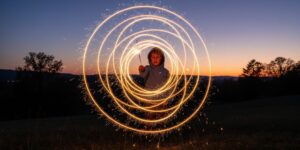 A young boy moves a sparkler in a circle to create a circle of light in a long exposure photo.