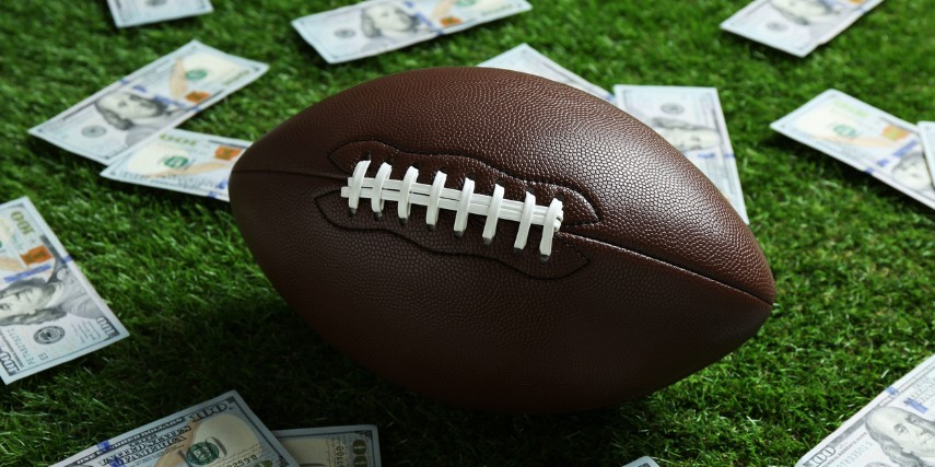 A football sits on turf with 100-dollar bills scattered around it.
