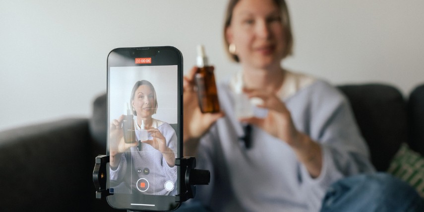 A woman records herself on a smartphone talking about a product while sitting on a couch.