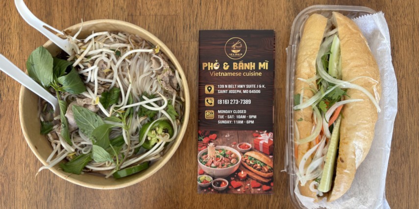 A bowl of Vietnamese food and a sub-style Vietnamese sandwich on a table with a menu for the restaurant in the center.