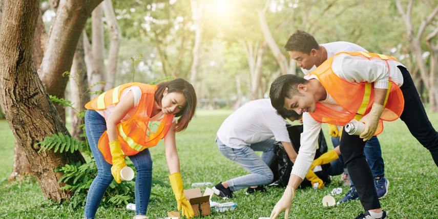 Volunteers wearing orange vests pick up trash in a park.