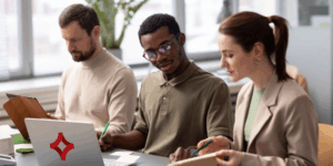 Three professionals sit at a table looking at information with an SJC logo on the laptop in front of them.