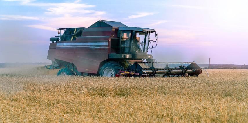 A combine harvests grain against a multi-colored harvest season sky.