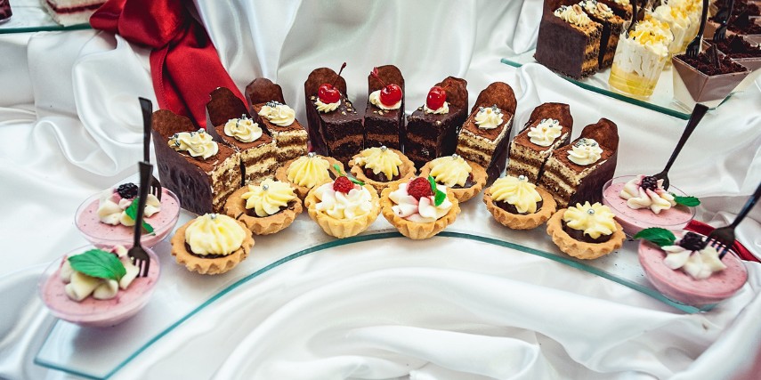 Two rows of fancy desserts are arranged on a glass half-circle on a white satin cloth.
