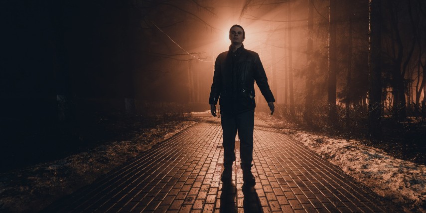 A backlit man walks down a cobblestone street in the dark.