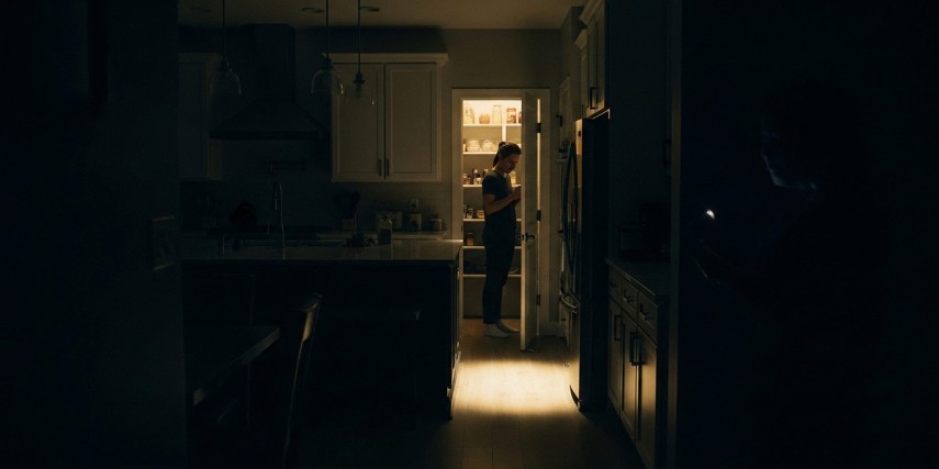 A woman stands in her pantry in a darkened house.