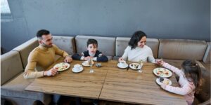 A father, mother and two children enjoy a meal together in a large restaurant banquette.