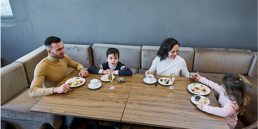 A father, mother and two children enjoy a meal together in a large restaurant banquette.