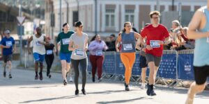 A group of runners makes their way up a hill in an urban setting, smiling at the camera.
