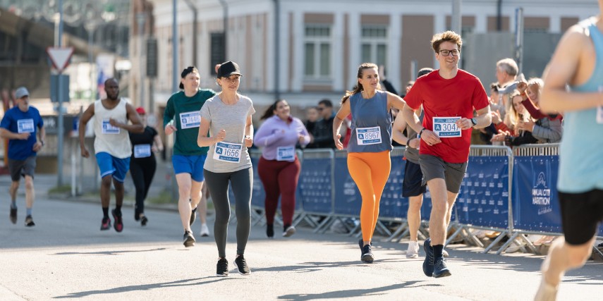 A group of runners makes their way up a hill in an urban setting, smiling at the camera.