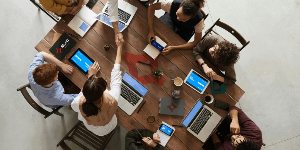 Aerial view of colleagues sitting at a table discussing partnership strategy surrounded by laptops and documents