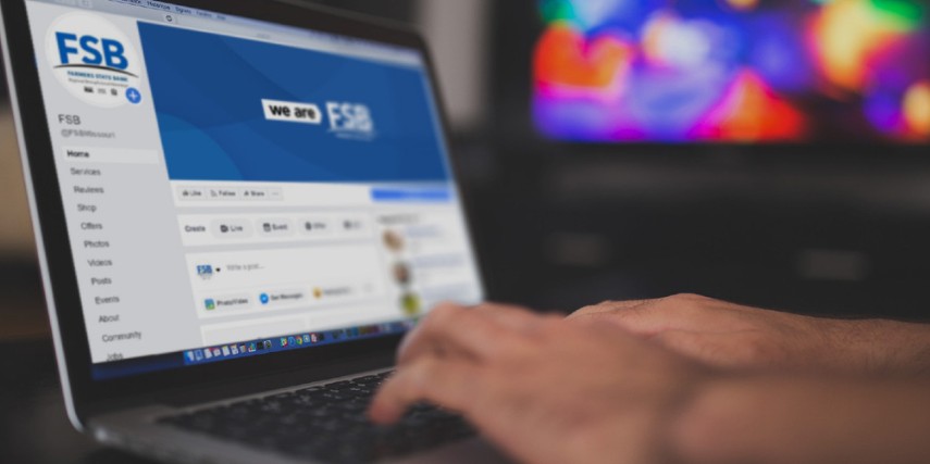 A person sits at a laptop, where a bank's social media profile is pulled up on the screen.